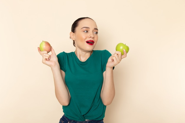 Vista frontal mujer joven en camisa verde oscuro y jeans con manzana y pera en beige