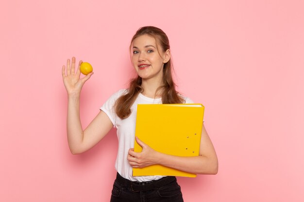 Vista frontal de la mujer joven en camiseta blanca con limón fresco con archivos en la pared rosa