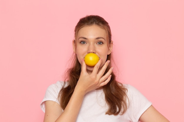 Vista frontal de la mujer joven en camiseta blanca con limón fresco sonriendo en la pared rosa