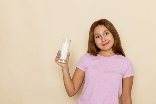 Vista frontal mujer joven en camiseta rosa y jeans azul sonriendo y bebiendo leche en gris