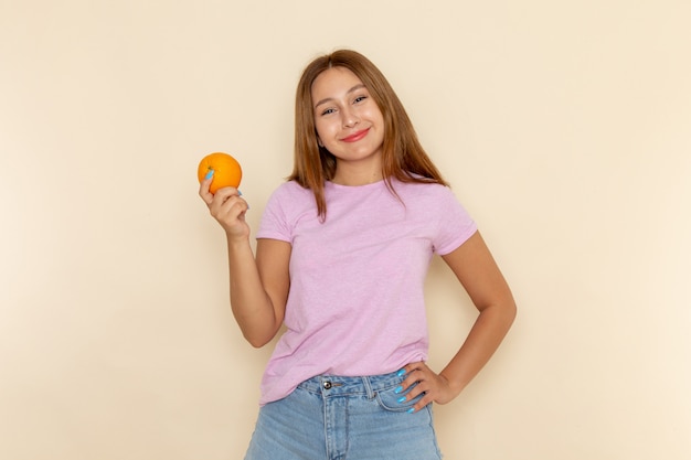 Vista frontal mujer joven en camiseta rosa y jeans azul sosteniendo naranja con una sonrisa en su rostro