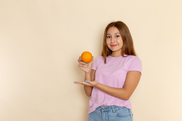 Vista frontal mujer joven en camiseta rosa y jeans con naranja con sonrisa