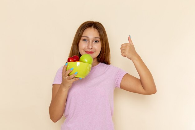 Vista frontal mujer joven en camiseta rosa y jeans sosteniendo plato con frutas sonriendo