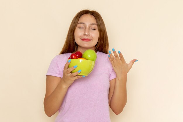 Vista frontal mujer joven en camiseta rosa y jeans sosteniendo plato con frutas