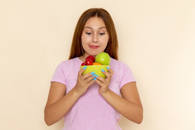 Vista frontal mujer joven en camiseta rosa y jeans sosteniendo plato con frutas