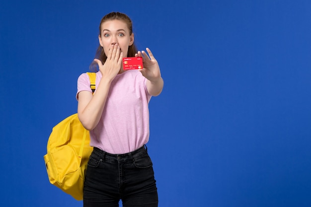 Vista frontal de la mujer joven en camiseta rosa con mochila amarilla con tarjeta roja de plástico