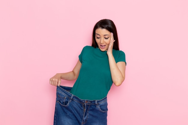 Vista frontal mujer joven en camiseta verde comprobando su cintura en la pared rosa cintura deporte ejercicio entrenamientos belleza mujer delgada