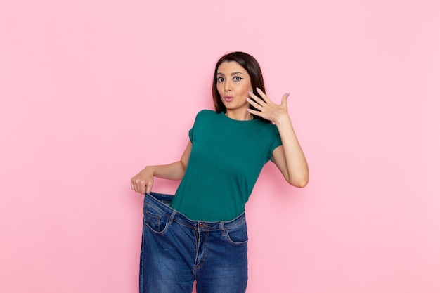 Vista frontal mujer joven en camiseta verde comprobando su cintura en la pared rosa cintura ejercicios deportivos entrenamientos belleza mujer delgada