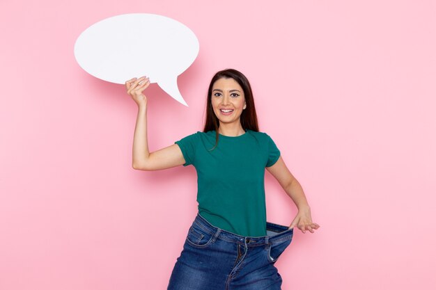 Vista frontal mujer joven en camiseta verde con enorme cartel blanco en la pared rosa cintura deporte ejercicio entrenamientos belleza atleta delgado