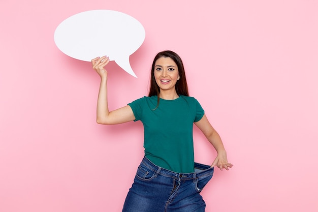 Vista frontal mujer joven en camiseta verde con enorme cartel blanco en la pared rosa cintura deporte ejercicio entrenamientos belleza atleta delgado