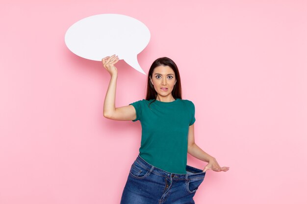 Vista frontal mujer joven en camiseta verde con gran cartel blanco en la pared rosa cintura deporte ejercicio entrenamiento belleza atleta delgado