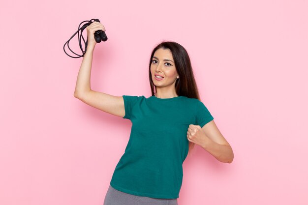 Foto gratuita vista frontal mujer joven en camiseta verde sosteniendo saltar la cuerda en la pared rosa claro cintura ejercicio entrenamiento belleza delgado deporte femenino