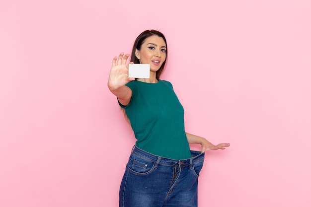 Foto gratuita vista frontal mujer joven en camiseta verde con tarjeta blanca en la pared rosa claro cintura deporte ejercicio entrenamientos belleza mujer delgada