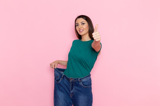 Vista frontal mujer joven en camiseta verde tocando sus jeans en la pared rosada cintura deporte ejercicio entrenamientos belleza atleta delgada