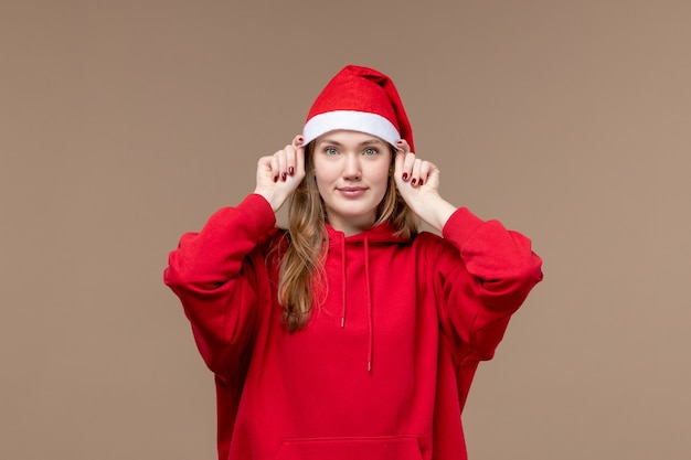 Vista frontal mujer joven con capa roja sonriendo sobre fondo marrón Navidad emoción vacaciones