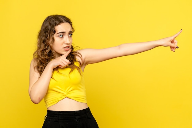 Vista frontal de la mujer joven con cara de miedo en la pared amarilla