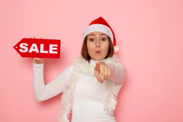 Foto gratuita vista frontal mujer joven celebración venta figura escrita en la pared rosa color navidad año nuevo vacaciones moda nieve