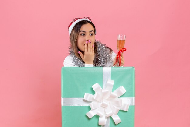 Vista frontal de la mujer joven celebrando la Navidad con bebida en la pared rosa