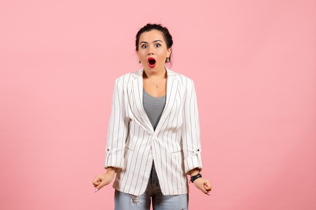 Vista frontal mujer joven con chaqueta blanca posando con cara de sorpresa sobre fondo rosa ropa dama emociones color moda mujer