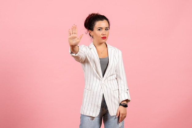 Vista frontal mujer joven con chaqueta blanca que muestra la señal de stop sobre fondo rosa dama moda mujer emociones color