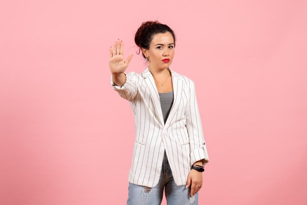 Vista frontal mujer joven con chaqueta blanca que muestra la señal de stop sobre fondo rosa dama moda mujer emociones color