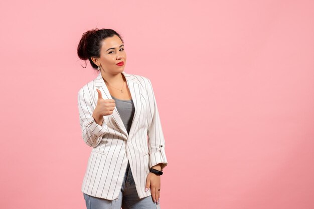 Vista frontal mujer joven con chaqueta blanca que muestra un signo impresionante sobre fondo rosa ropa dama emociones color moda mujer