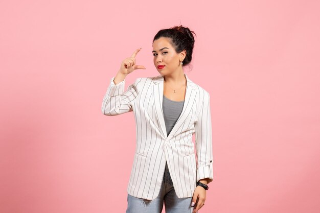 Vista frontal mujer joven con chaqueta blanca que muestra el tamaño sobre fondo rosa dama moda mujer emoción color