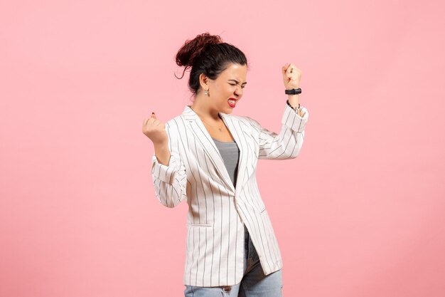 Vista frontal mujer joven con chaqueta blanca regocijándose emocionalmente sobre fondo rosa ropa dama emociones color moda mujer