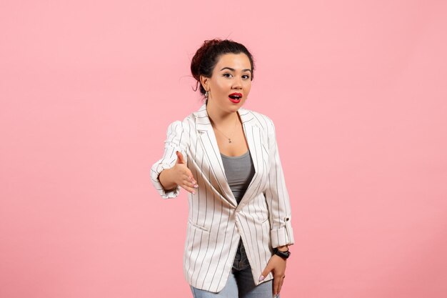 Vista frontal mujer joven con chaqueta blanca tratando de estrechar la mano sobre fondo rosa dama moda mujer emociones color