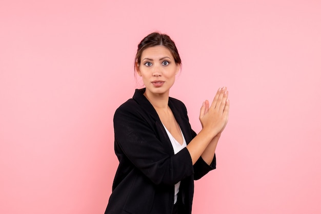 Vista frontal mujer joven en chaqueta oscura aplaudiendo sobre fondo rosa