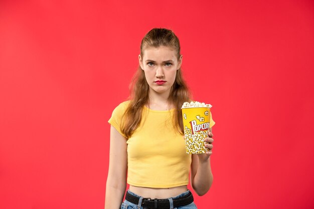 Vista frontal mujer joven en el cine con paquete de palomitas de maíz con expresión deprimida en la pared roja películas cine cine cine