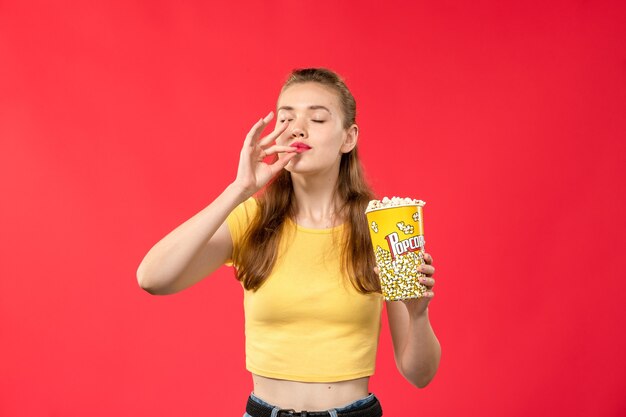 Vista frontal mujer joven en el cine con paquete de palomitas de maíz en la pared roja clara películas cine cine cine