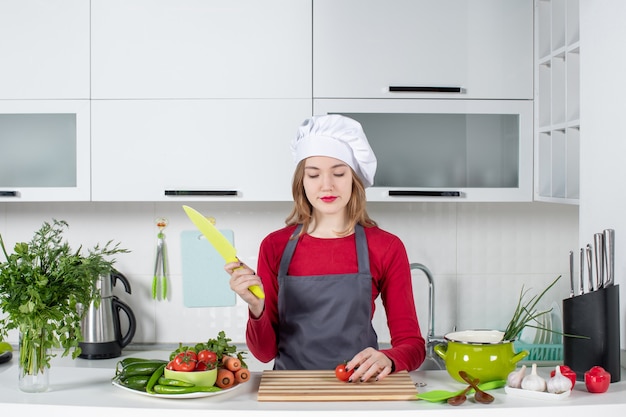 Vista frontal, mujer joven, cocinero, en, delantal, picar, tomate colección de foto