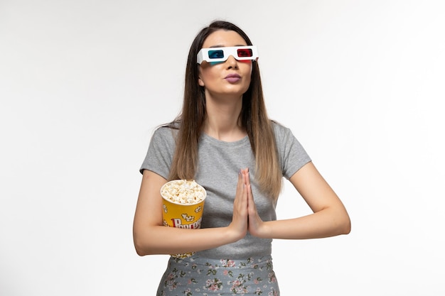 Vista frontal mujer joven comiendo palomitas de maíz y viendo películas en gafas de sol d en escritorio blanco