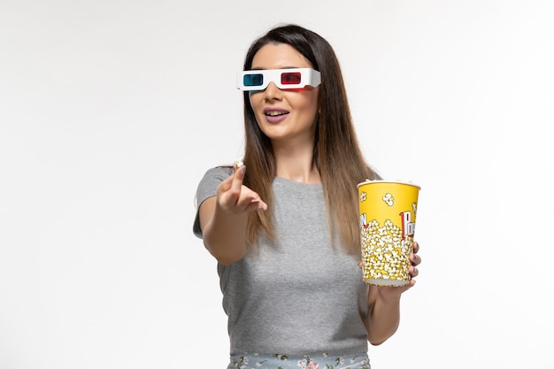 Vista frontal mujer joven comiendo palomitas de maíz y viendo películas en gafas de sol d sobre la superficie blanca clara
