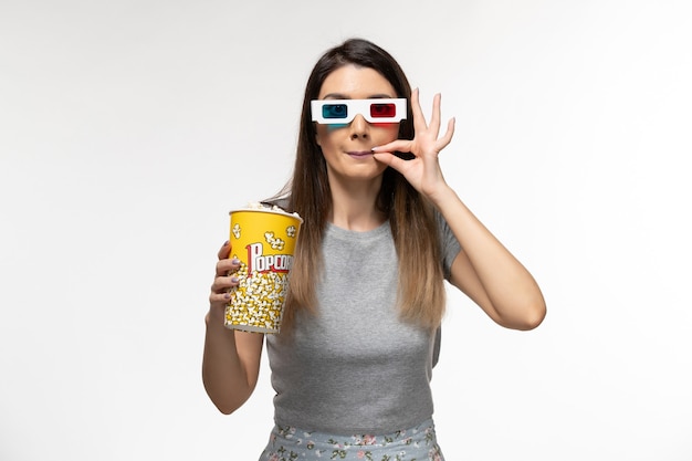 Vista frontal mujer joven comiendo palomitas de maíz y viendo películas en gafas de sol d sobre la superficie blanca clara