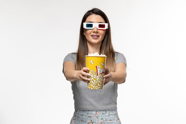 Vista frontal mujer joven comiendo palomitas de maíz y viendo películas en gafas de sol d sobre la superficie blanca clara