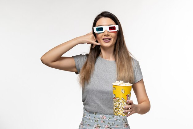 Vista frontal mujer joven comiendo palomitas de maíz y viendo películas en gafas de sol d sobre superficie blanca