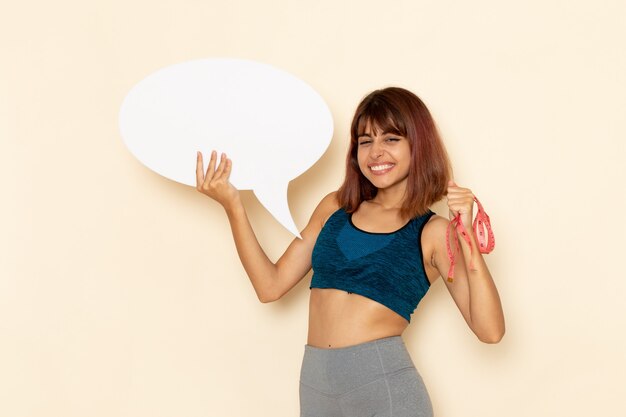 Vista frontal de la mujer joven con cuerpo en forma en camisa azul con cartel blanco en la pared blanca