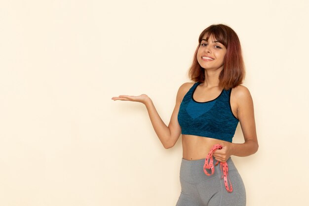 Vista frontal de la mujer joven con cuerpo en forma en camisa azul sonriendo en la pared de color blanco claro