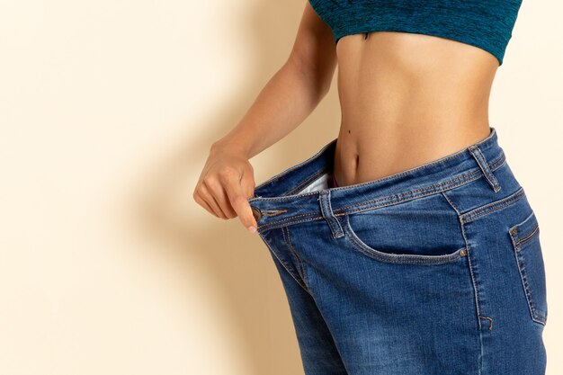 Vista frontal de la mujer joven con cuerpo en forma en camisa y jeans en la pared blanca