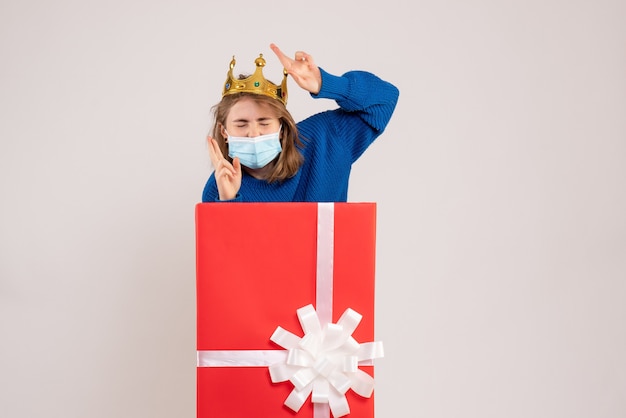 Foto gratuita vista frontal de la mujer joven dentro de la caja de regalo en máscara en la pared blanca