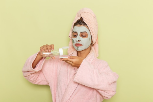 Vista frontal mujer joven después de la ducha en bata de baño rosa con desmaquillador sobre superficie verde