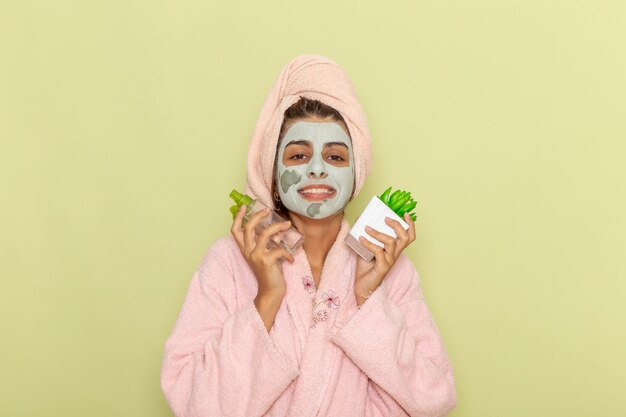 Vista frontal mujer joven después de la ducha en bata de baño rosa con desmaquilladores sonriendo sobre superficie verde