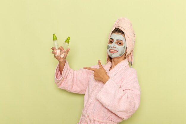 Vista frontal mujer joven después de la ducha en bata de baño rosa con desmaquilladores sonriendo sobre superficie verde