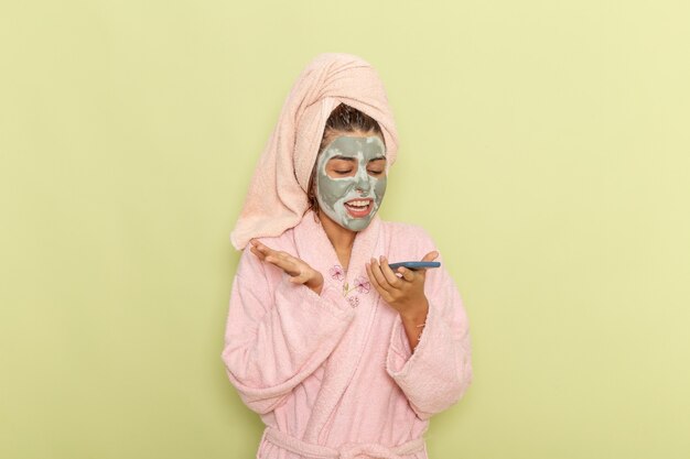 Vista frontal mujer joven después de la ducha en bata de baño rosa hablando por teléfono en la superficie verde