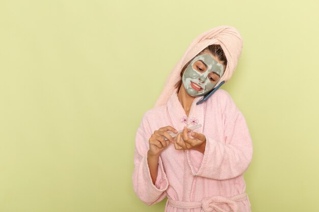 Vista frontal mujer joven después de la ducha en bata de baño rosa hablando por teléfono en la superficie verde