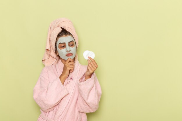 Vista frontal mujer joven después de la ducha en bata de baño rosa sosteniendo rondas de algodón sobre superficie verde