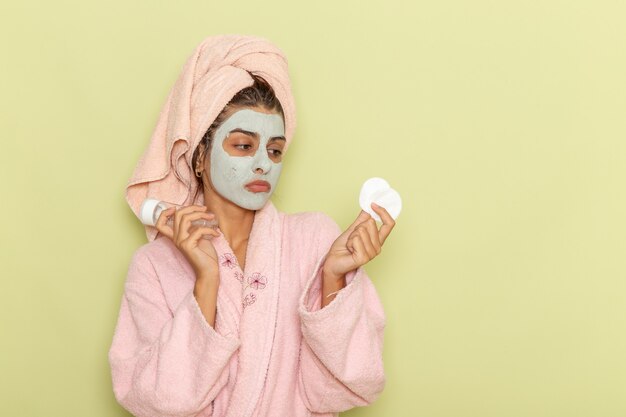 Foto gratuita vista frontal mujer joven después de la ducha en bata de baño rosa con spray y algodón sobre superficie verde