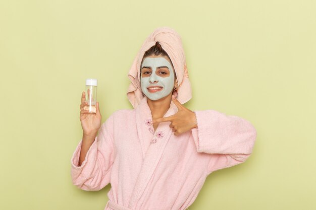Vista frontal mujer joven después de la ducha en bata de baño rosa con spray sobre una superficie verde